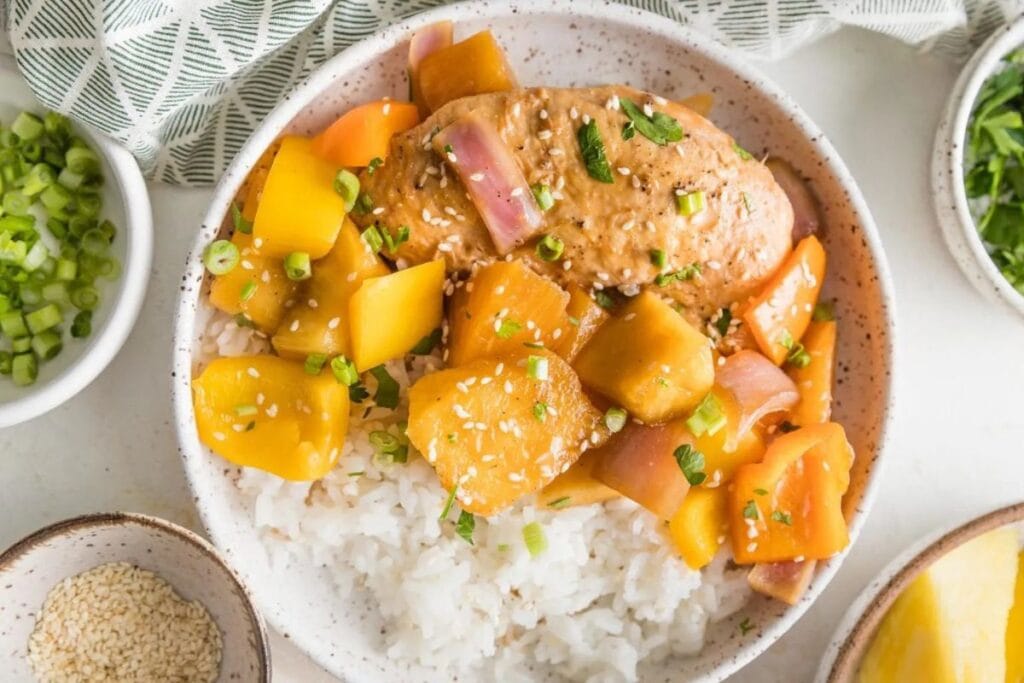 Chicken and pineapple chunks over rice, garnished with sesame seeds and green onions.