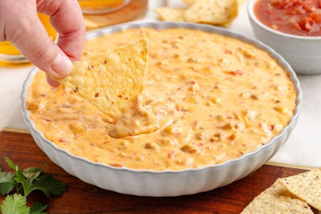 Tortilla chip being dipped into a bowl of creamy Rotel sausage dip.