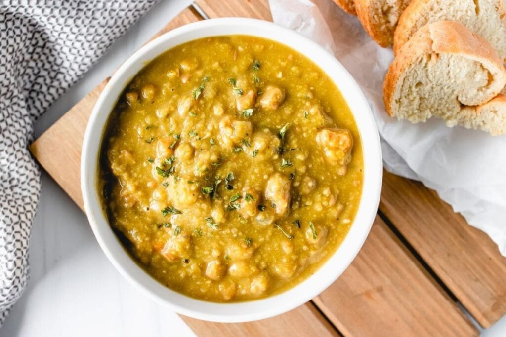 Overhead shot of split pea soup with ham, garnished with herbs, served with bread.