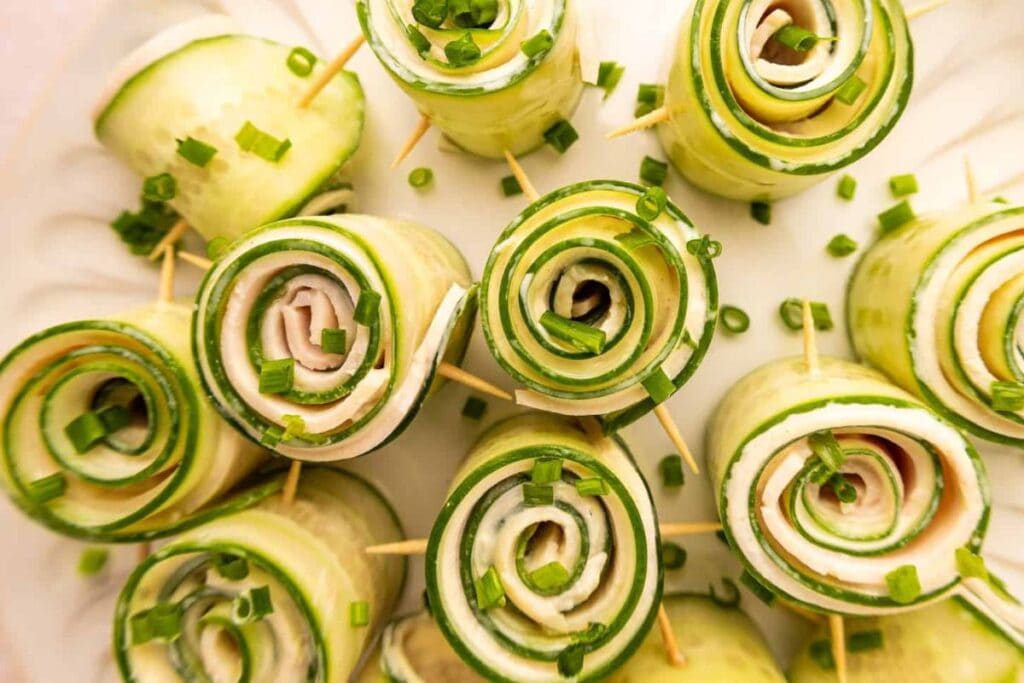 Cucumber roll-ups filled with cream cheese and ham, garnished with chives and secured with toothpicks.