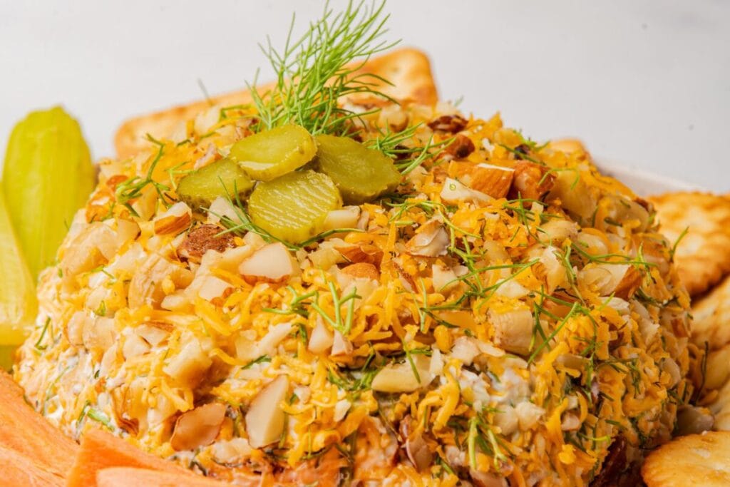 Cheese ball with dill, pickles, almonds, and cheddar cheese, served with crackers, celery, and carrots.