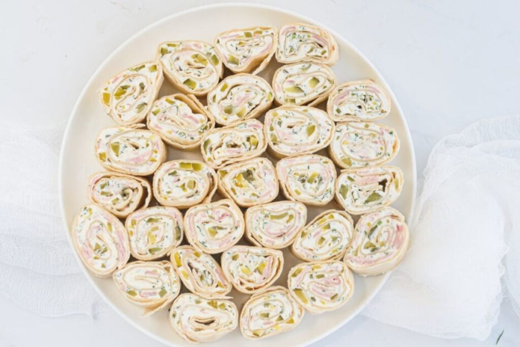 Tortilla pinwheels with cream cheese, ham, and pickles on a white plate.