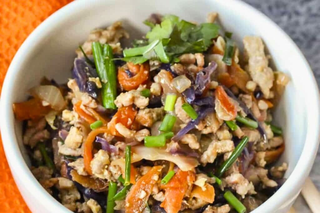 Egg roll in a bowl with ground meat, cabbage, carrots, and green onions.