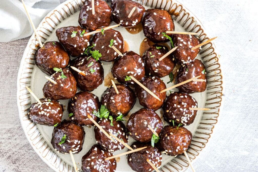Meatballs with grape jelly glaze, sesame seeds, and toothpicks on a decorative plate.