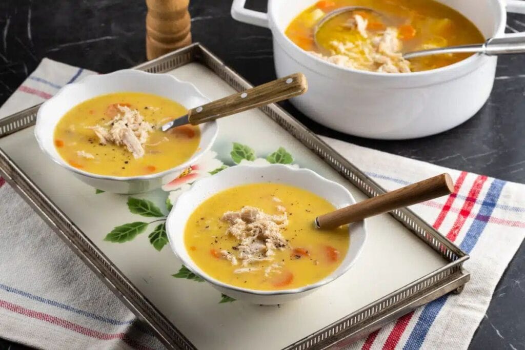 Bowls of Greek chicken soup on a floral tray with pot in background.