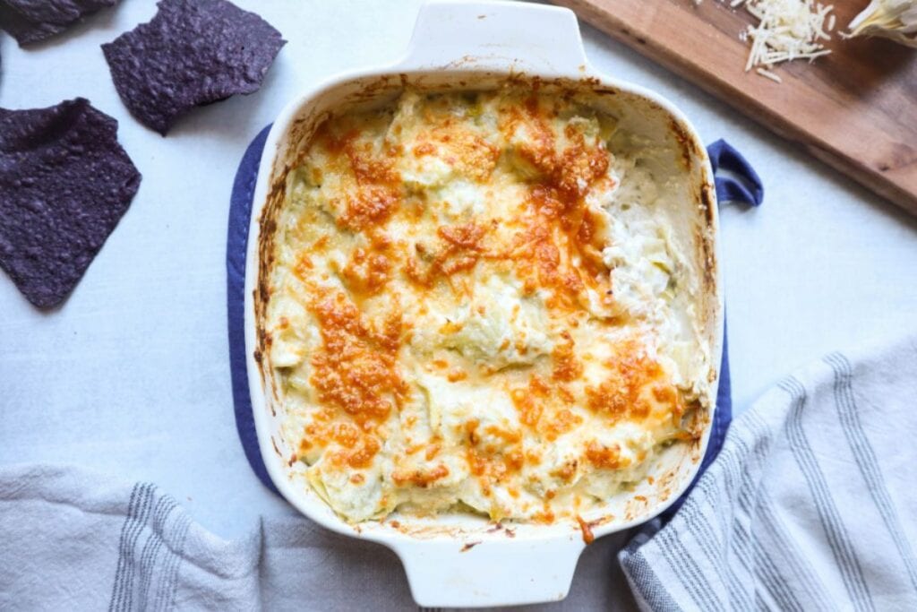 Green chile artichoke dip with melted cheese and blue corn chips.