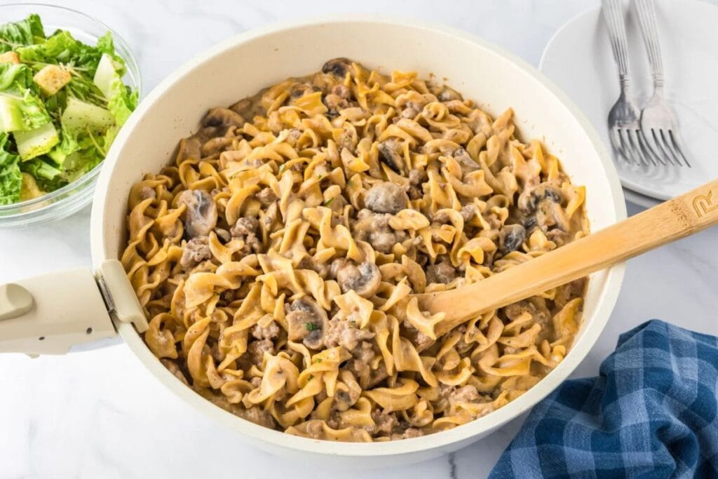 Beef stroganoff with egg noodles and mushrooms in a skillet, served with salad.