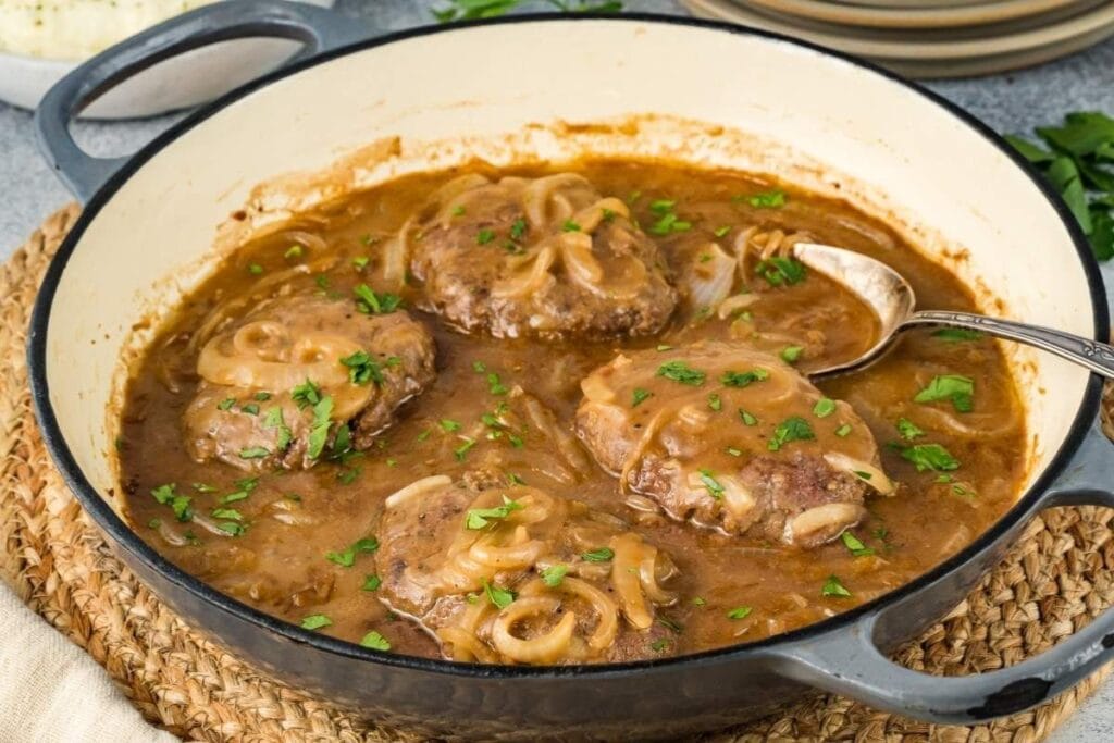 Hamburger steaks with gravy and onions in a skillet, garnished with parsley.