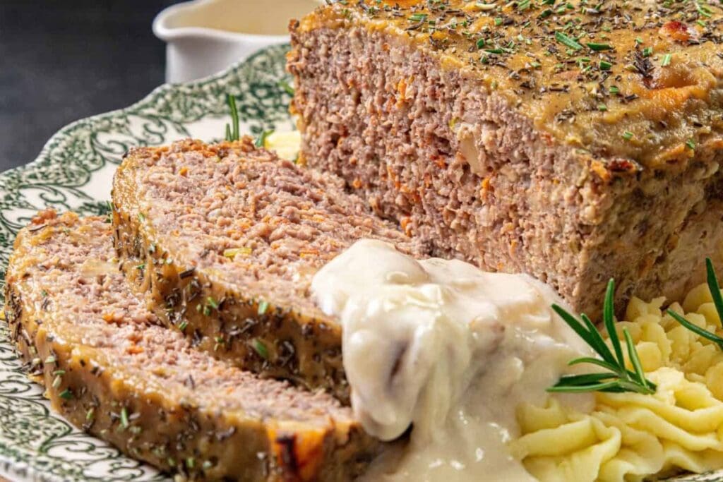 Sliced meatloaf on a plate with gravy and mashed potatoes.
