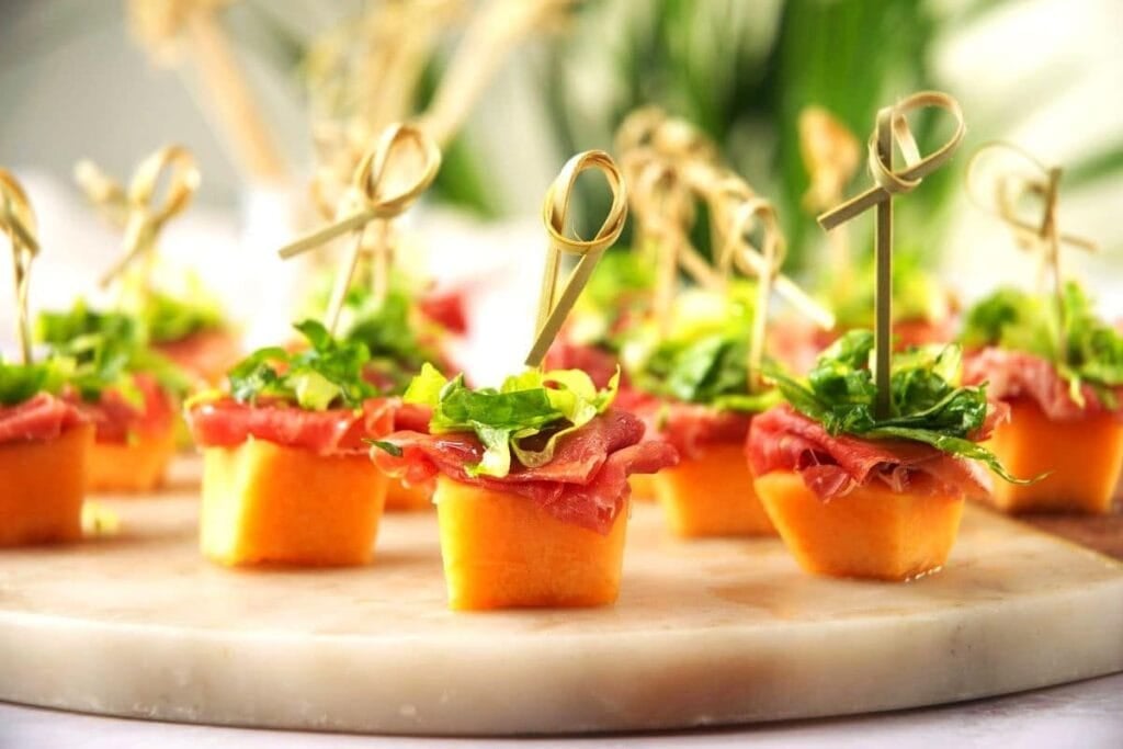 Cantaloupe bites topped with prosciutto and greens, skewered on a platter.