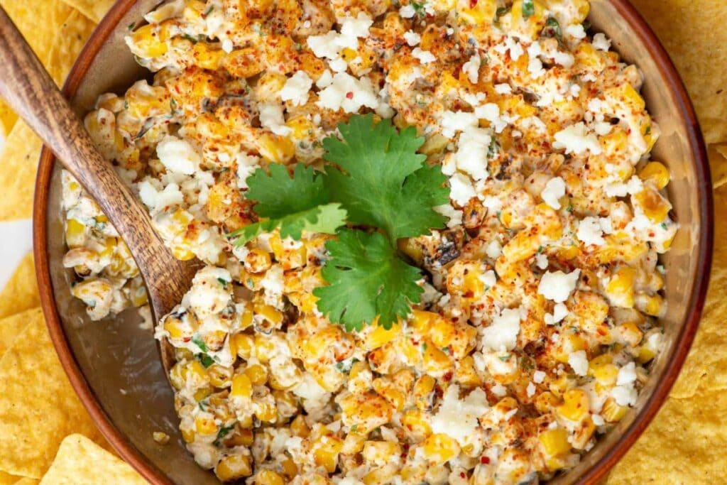 Mexican street corn dip in a bowl with a wooden spoon and tortilla chips.