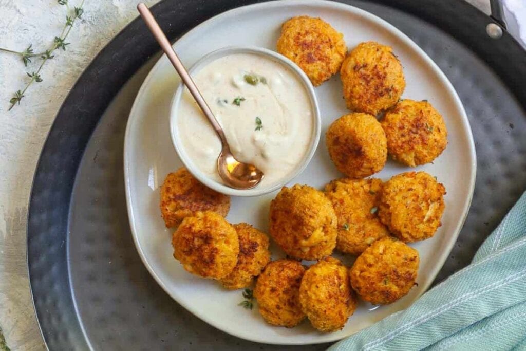Crab cakes on a plate with dipping sauce and a spoon.
