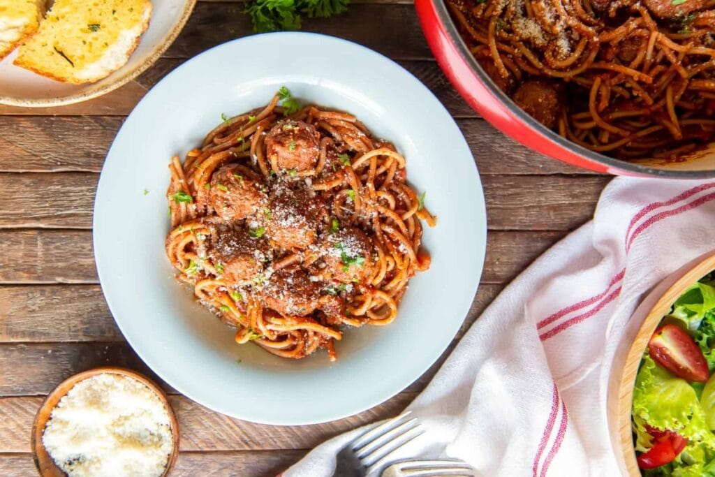 Overhead shot of spaghetti and meatballs on a plate with garlic bread and salad.