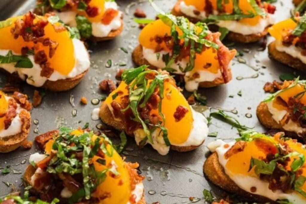 Crostini topped with ricotta cheese, peaches, bacon, and basil on a tray.
