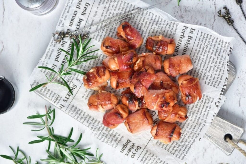 Pigs in a blanket on a newspaper-lined cutting board with rosemary sprigs.