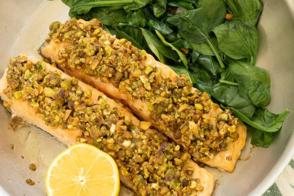 Pistachio-crusted salmon fillets served with spinach and a lemon wedge.