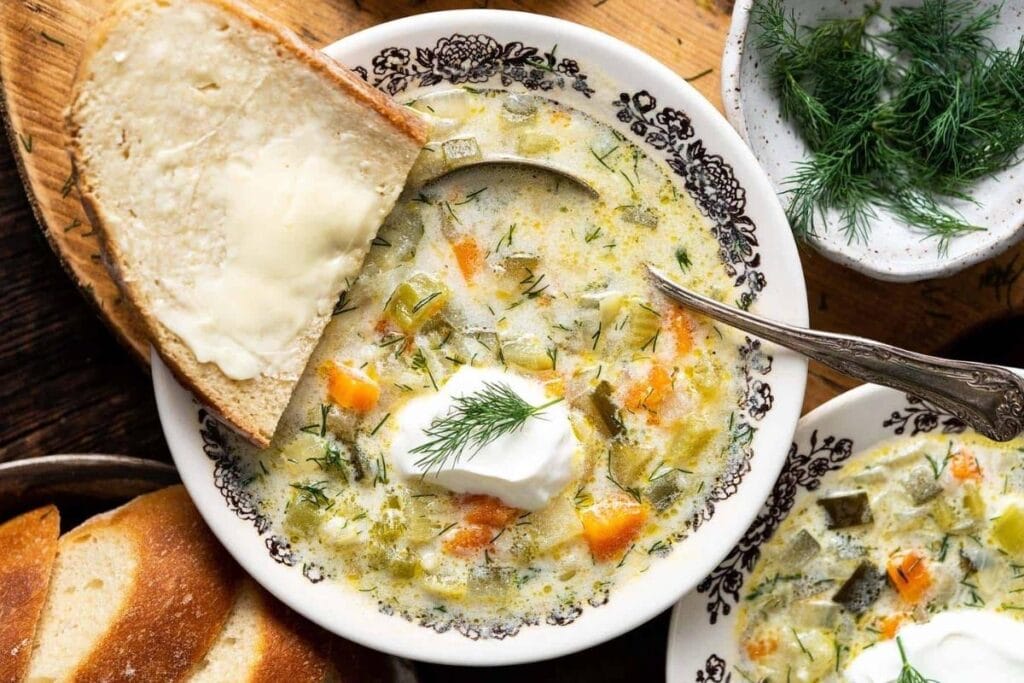 Overhead shot of Polish dill pickle soup with sour cream and buttered bread.