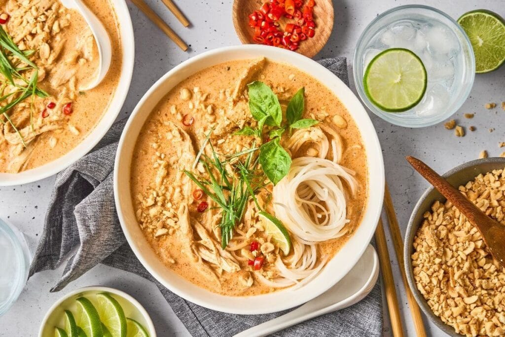Overhead shot of red curry chicken noodle soup with peanuts and lime.