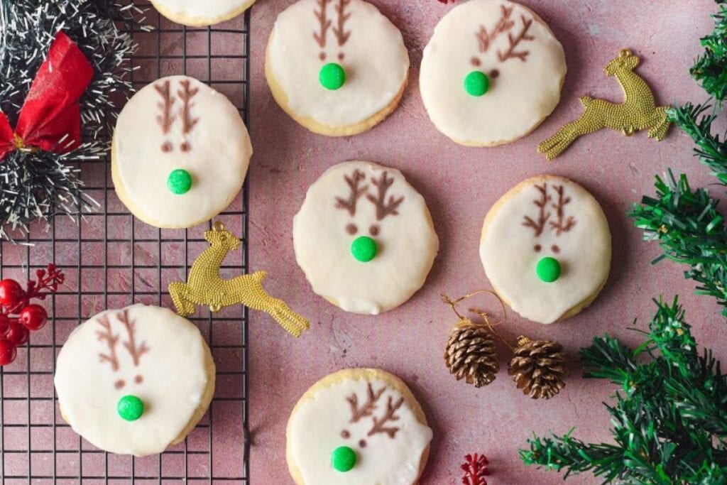 Overhead shot of reindeer cookies with white icing, green candy noses, and antler decorations.