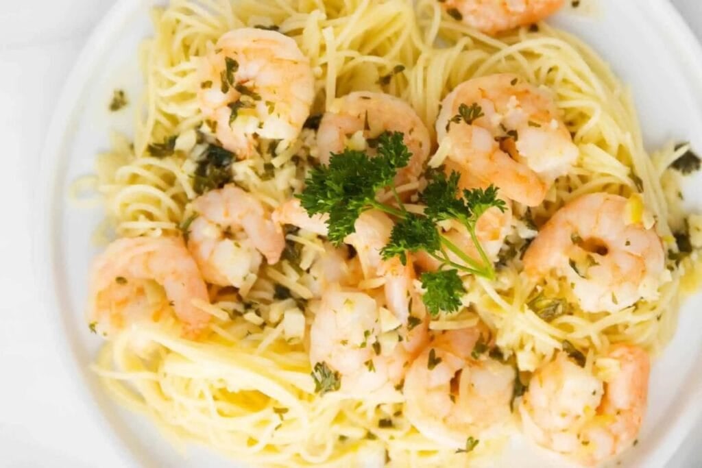 Angel hair pasta with shrimp scampi and parsley on a white plate.