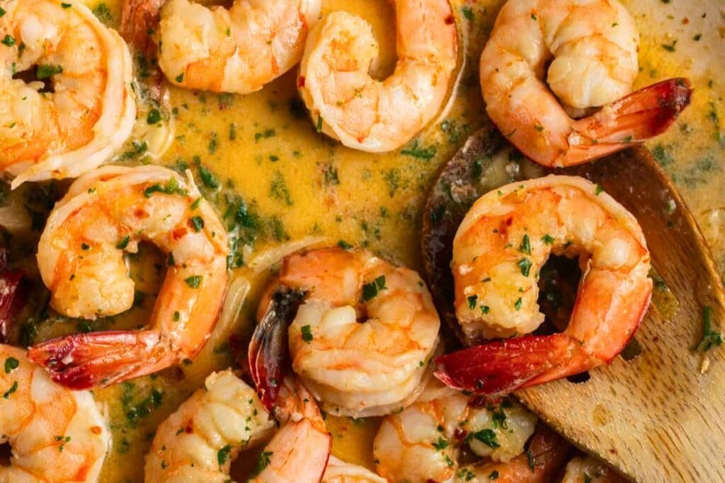 Close-up of shrimp scampi with herbs and a wooden spoon.