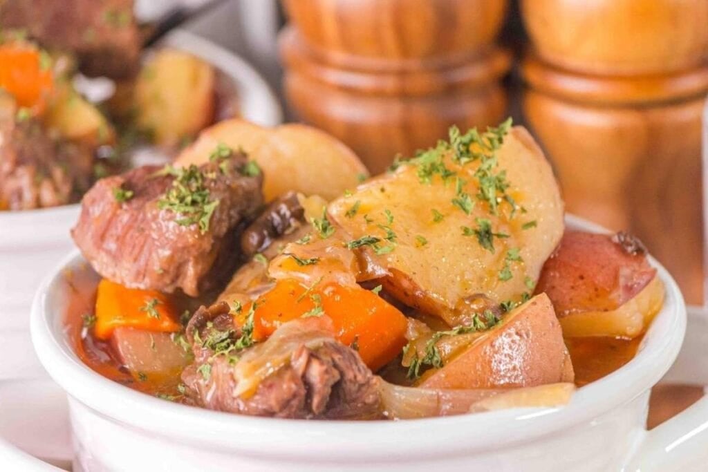 Beef stew with potatoes, carrots, and onions in a white bowl, garnished with parsley.