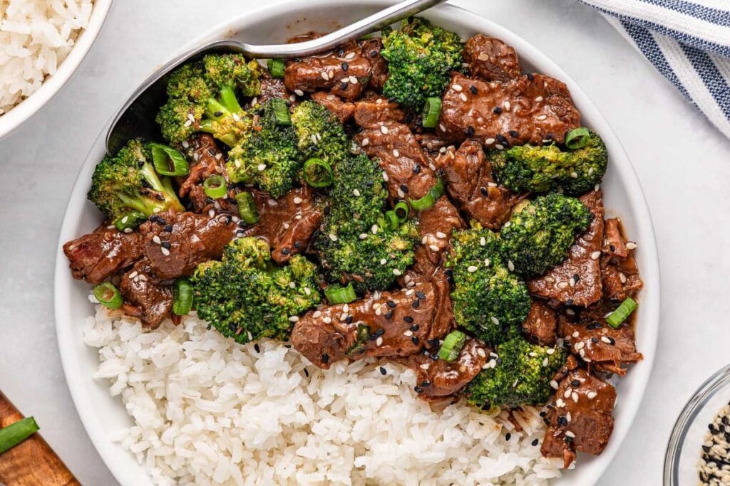 Beef and broccoli stir-fry over white rice, garnished with sesame seeds and scallions.