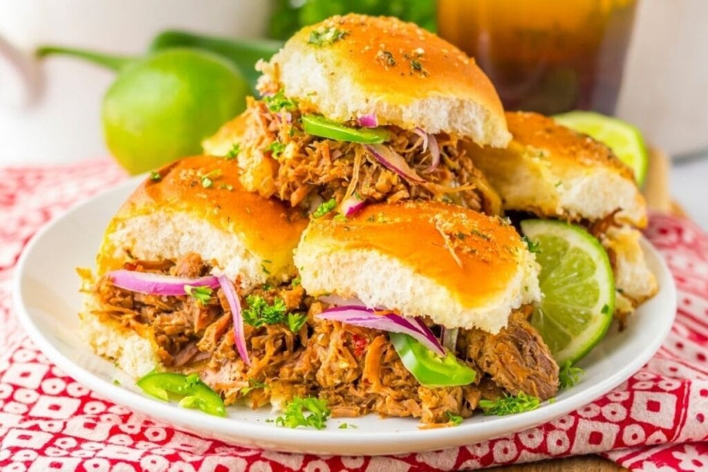 Pulled pork sliders with red onion, jalapeño, and lime on a white plate.