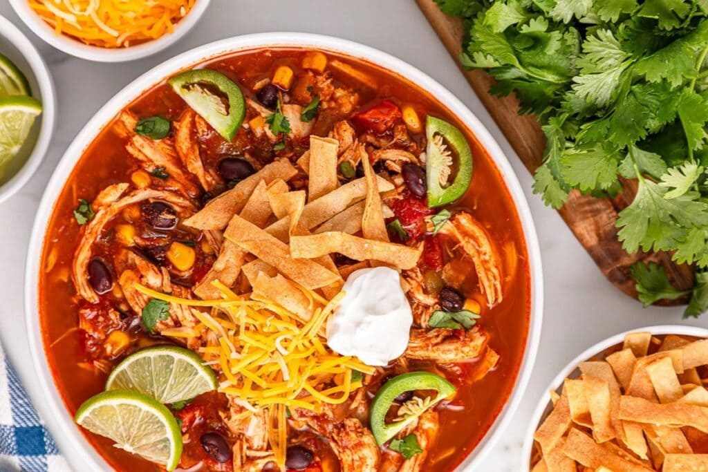 Overhead shot of chicken tortilla soup with toppings like tortilla strips and lime.