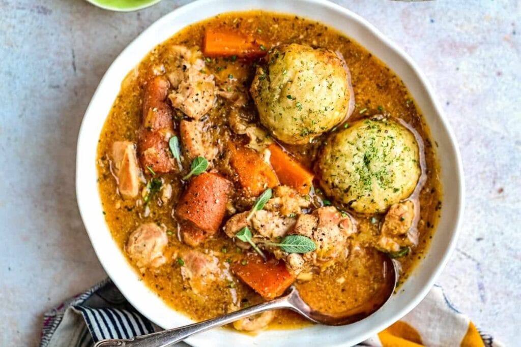 Overhead shot of chicken and dumplings with carrots in a white bowl.