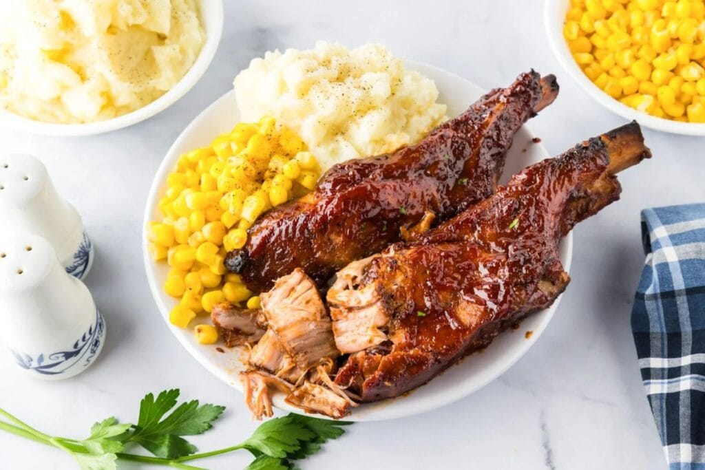 Pork ribs with BBQ sauce, mashed potatoes, and corn on a white plate.