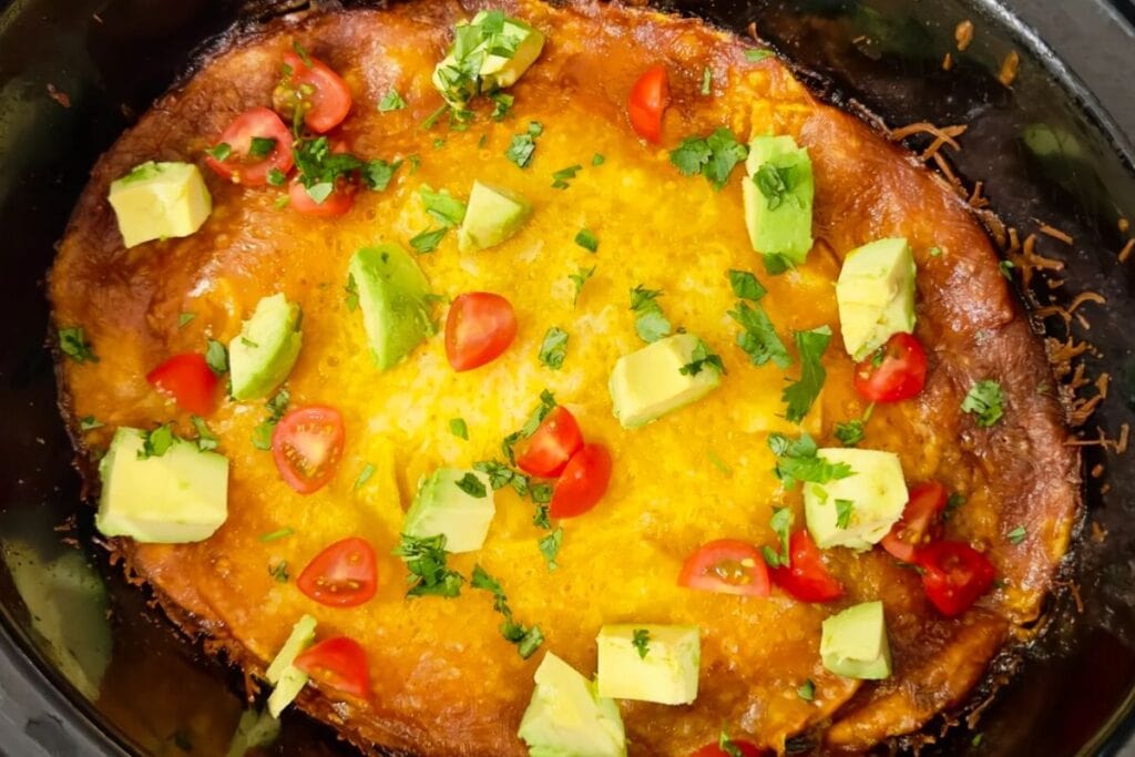 Overhead shot of layered beef enchiladas with avocado, tomatoes, and cilantro.