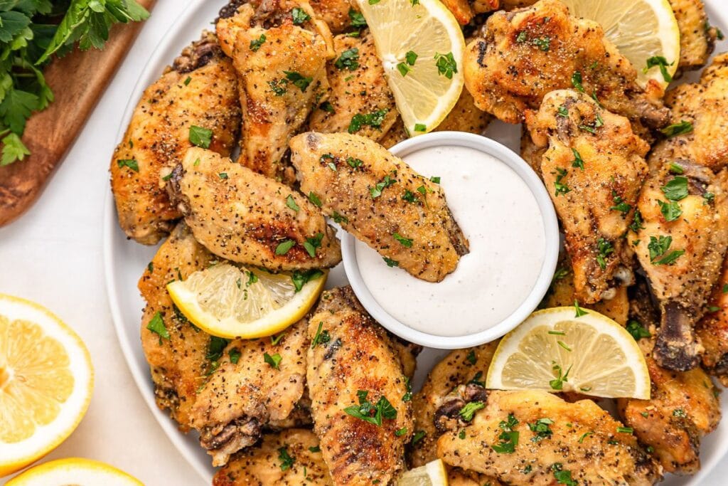 Lemon pepper chicken wings on a plate with lemon slices and dipping sauce.