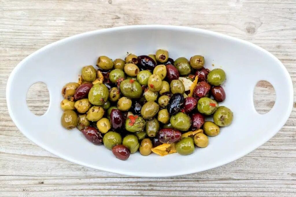 Assorted olives in a white serving dish on a wooden surface.