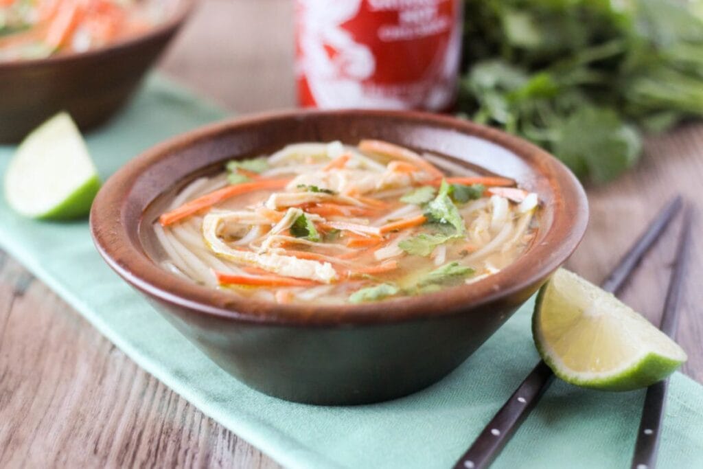 Bowl of Thai chicken noodle soup with lime wedge and chopsticks.