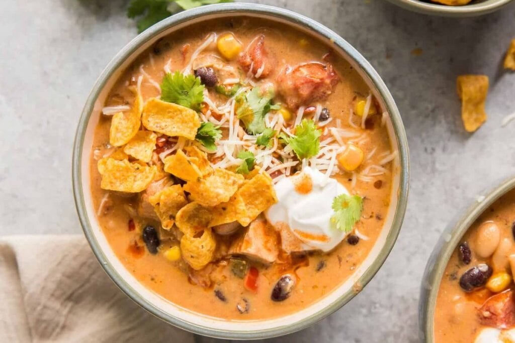 Bowl of creamy soup topped with tortilla chips, cheese, sour cream, and cilantro.