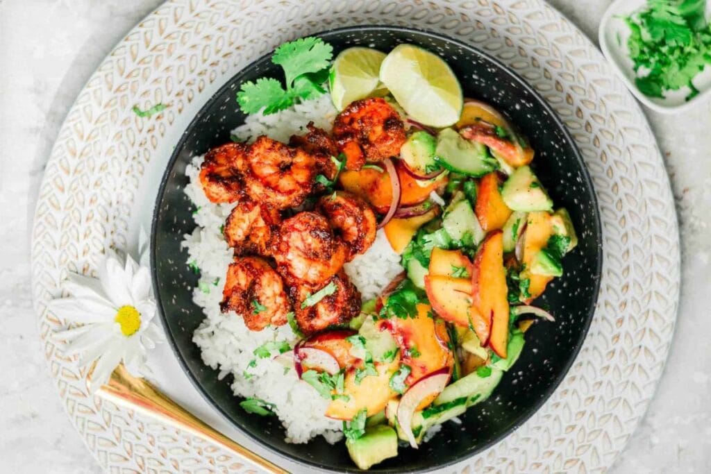 Black bowl with rice, spicy shrimp, peach avocado salad, lime, and cilantro.
