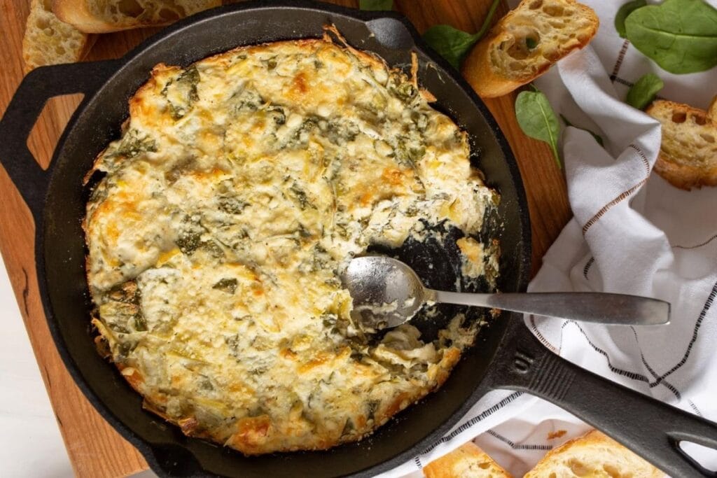 Spinach artichoke dip in a skillet with bread slices and a spoon.
