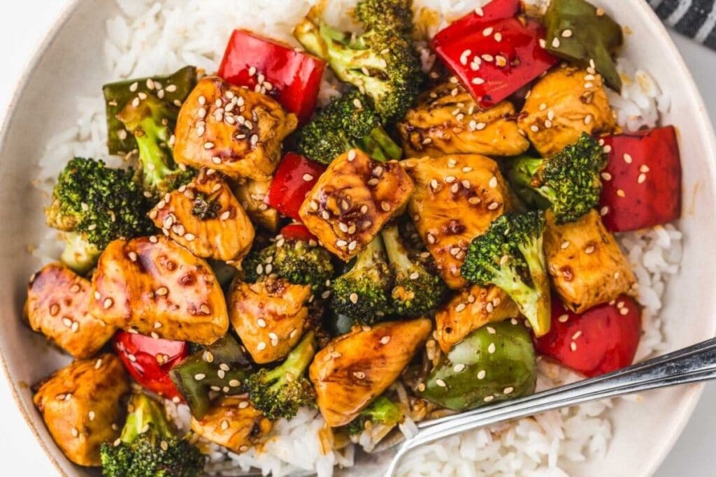 Teriyaki chicken and vegetables stir-fry over white rice, garnished with sesame seeds.