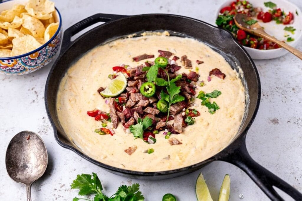 Queso dip in a cast iron skillet, topped with brisket, cilantro, and jalape&ntilde;os.