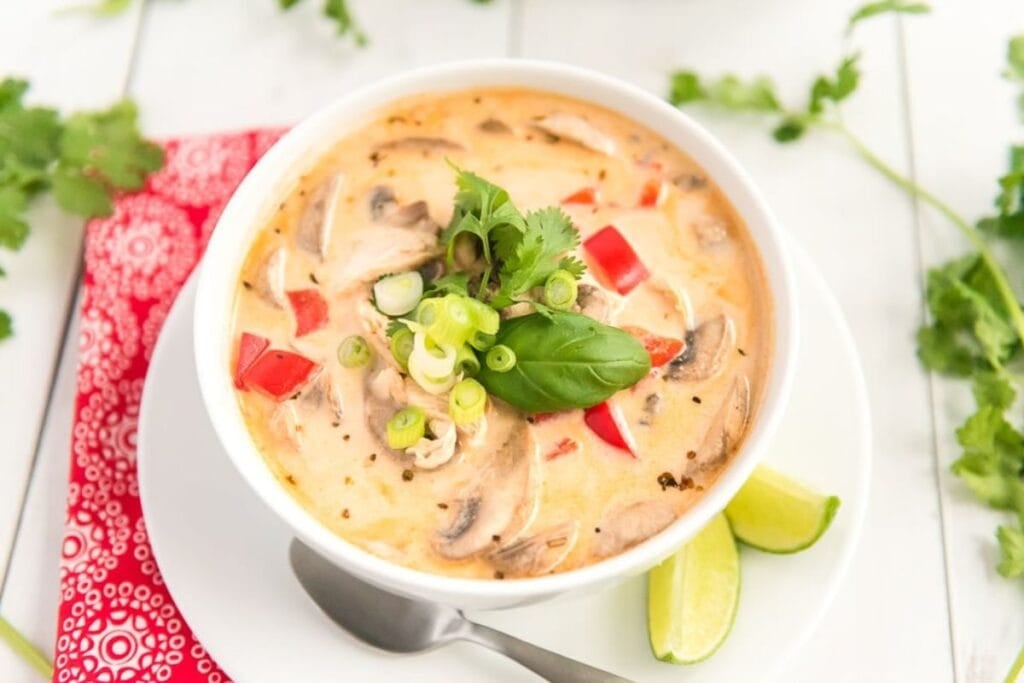 Creamy soup with mushrooms, red peppers, and green onions in a white bowl.