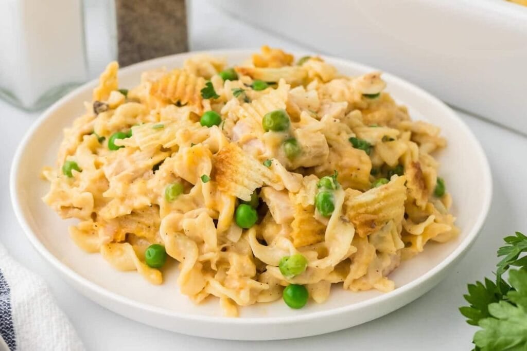 Tuna casserole with egg noodles, peas, and potato chip topping on a white plate.