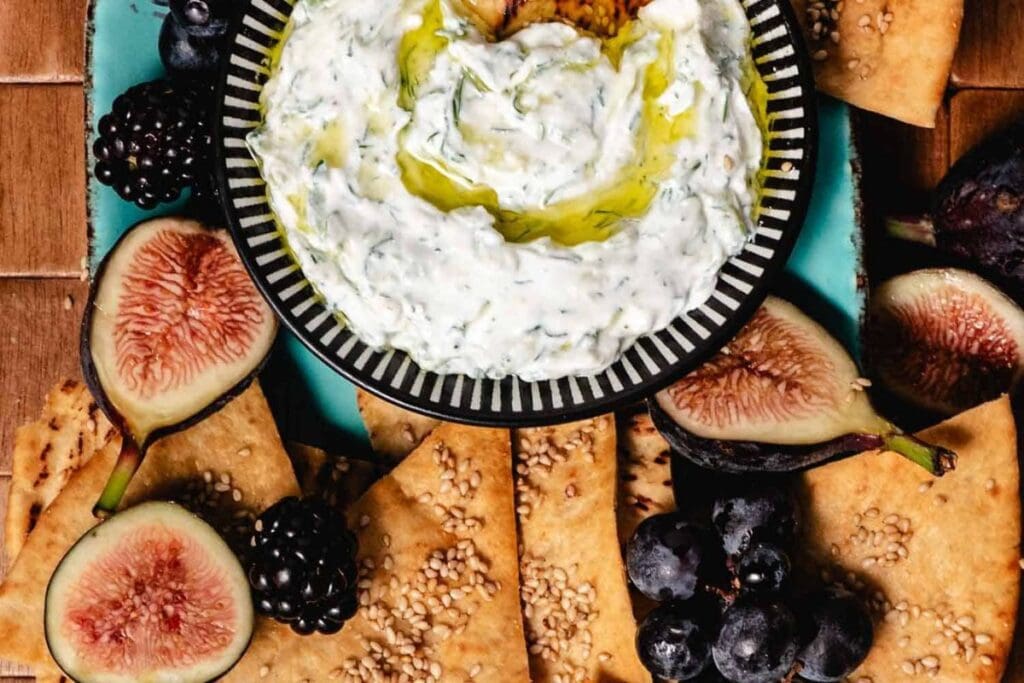 Tzatziki dip surrounded by pita chips, figs, blackberries, and grapes.