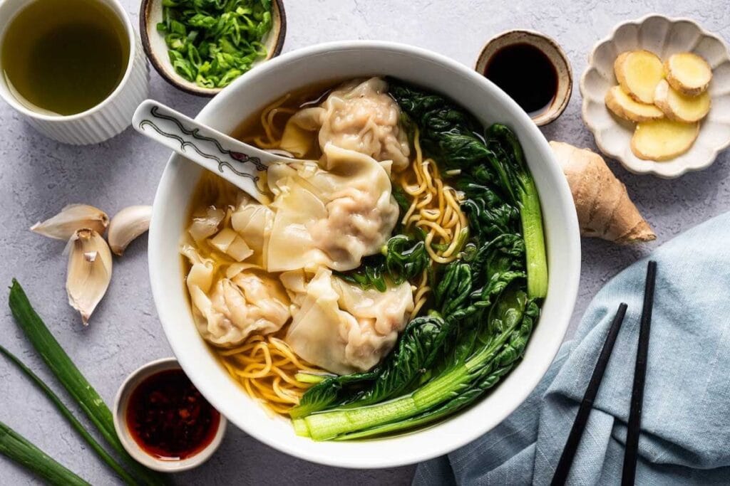 Overhead shot of wonton noodle soup with bok choy and condiments.