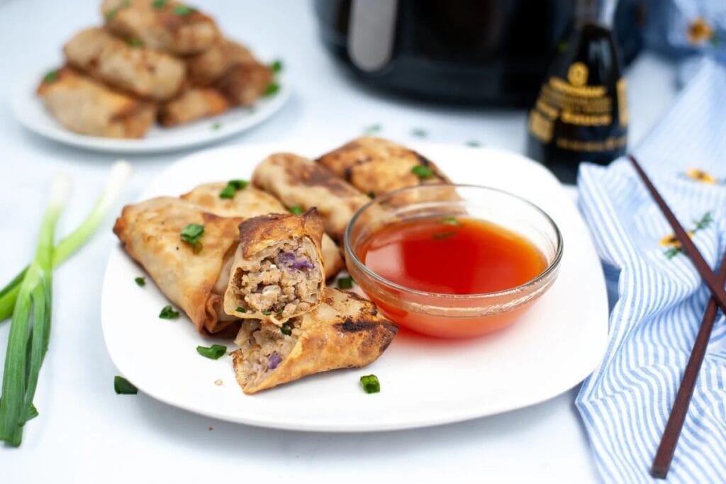 Air fryer egg rolls on a plate with dipping sauce.