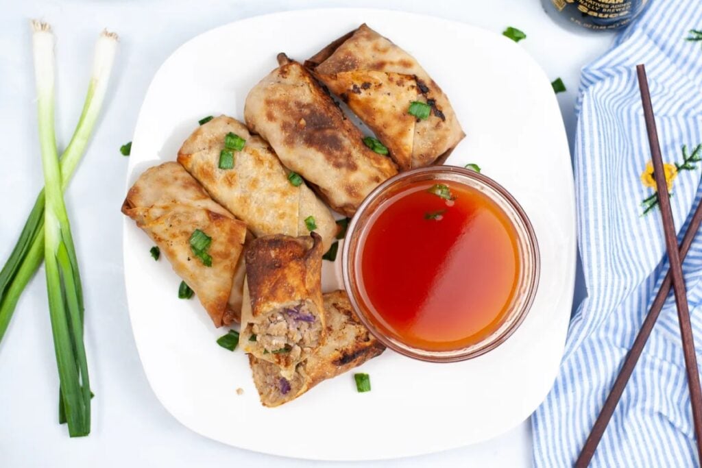 Egg rolls served on a plate with dipping sauce.