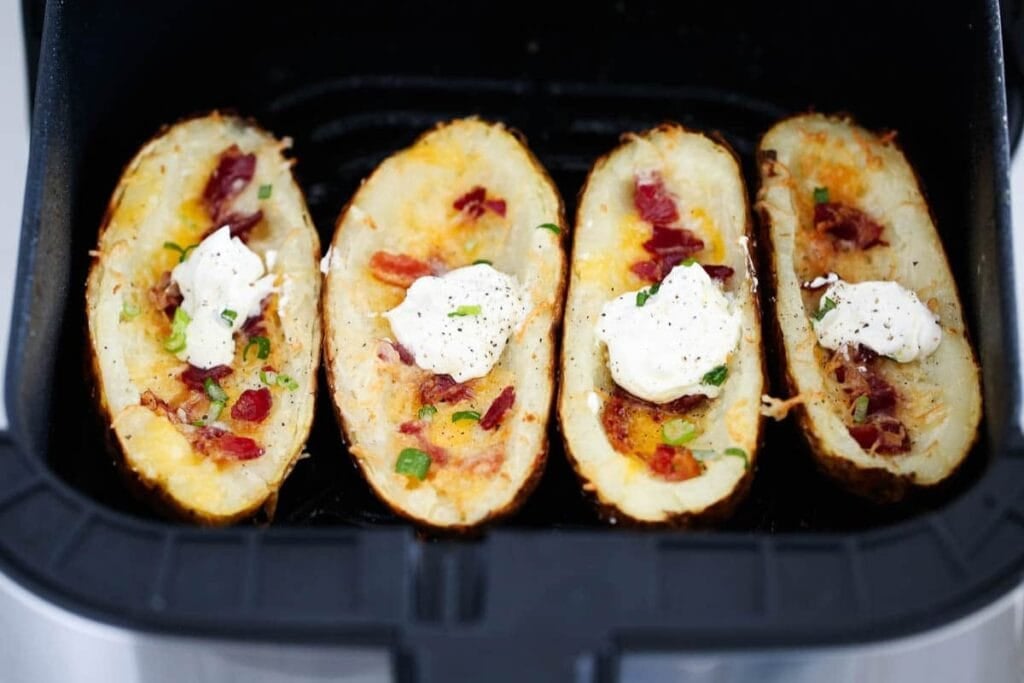 Potato skins loaded with cheese and bacon in an air fryer basket.