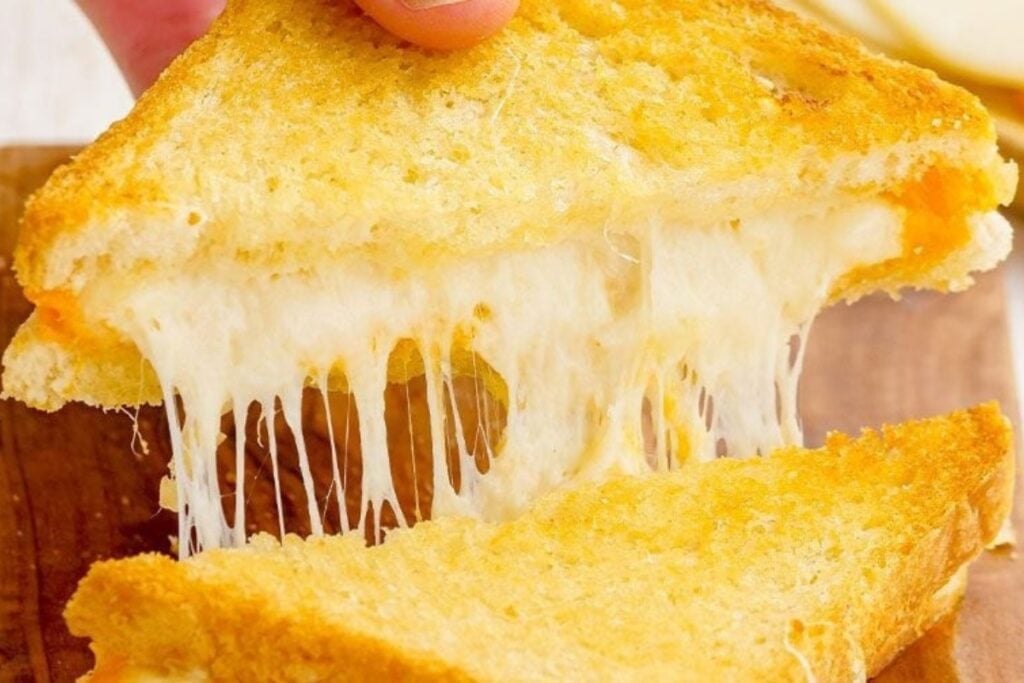 Close-up of baked grilled cheese sandwich sliced in half, showing melted cheese inside.