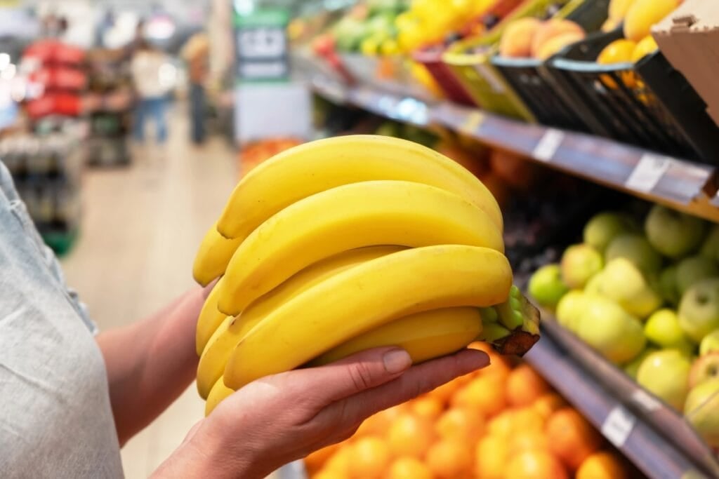 Hand holding a bunch of yellow bananas at the market.