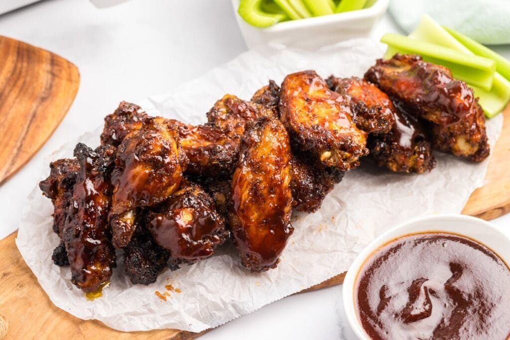 BBQ chicken wings on a wooden board with dipping sauce.